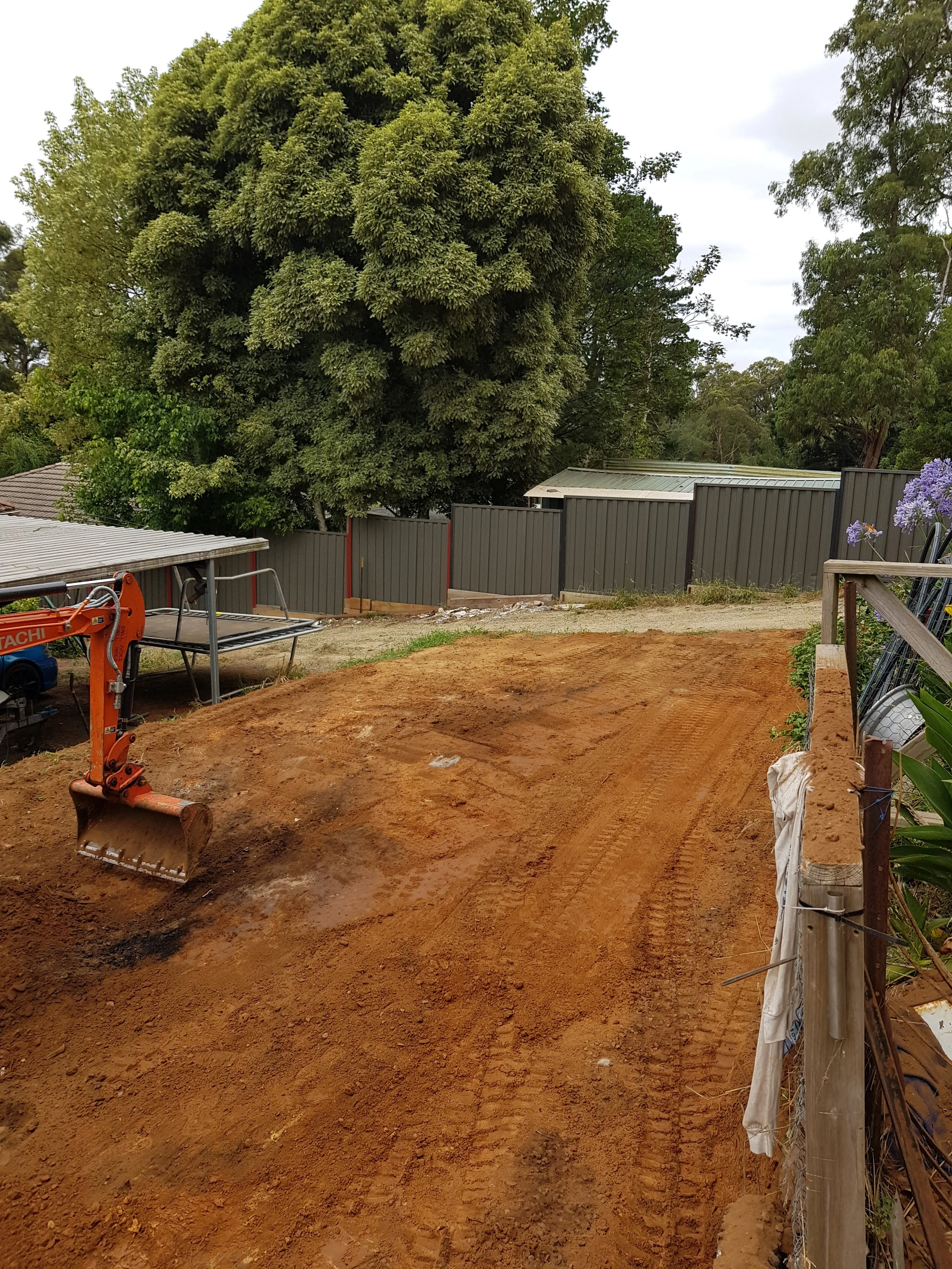 Levelled red clay backyard after the cut, with the mini excavator parked to one side.