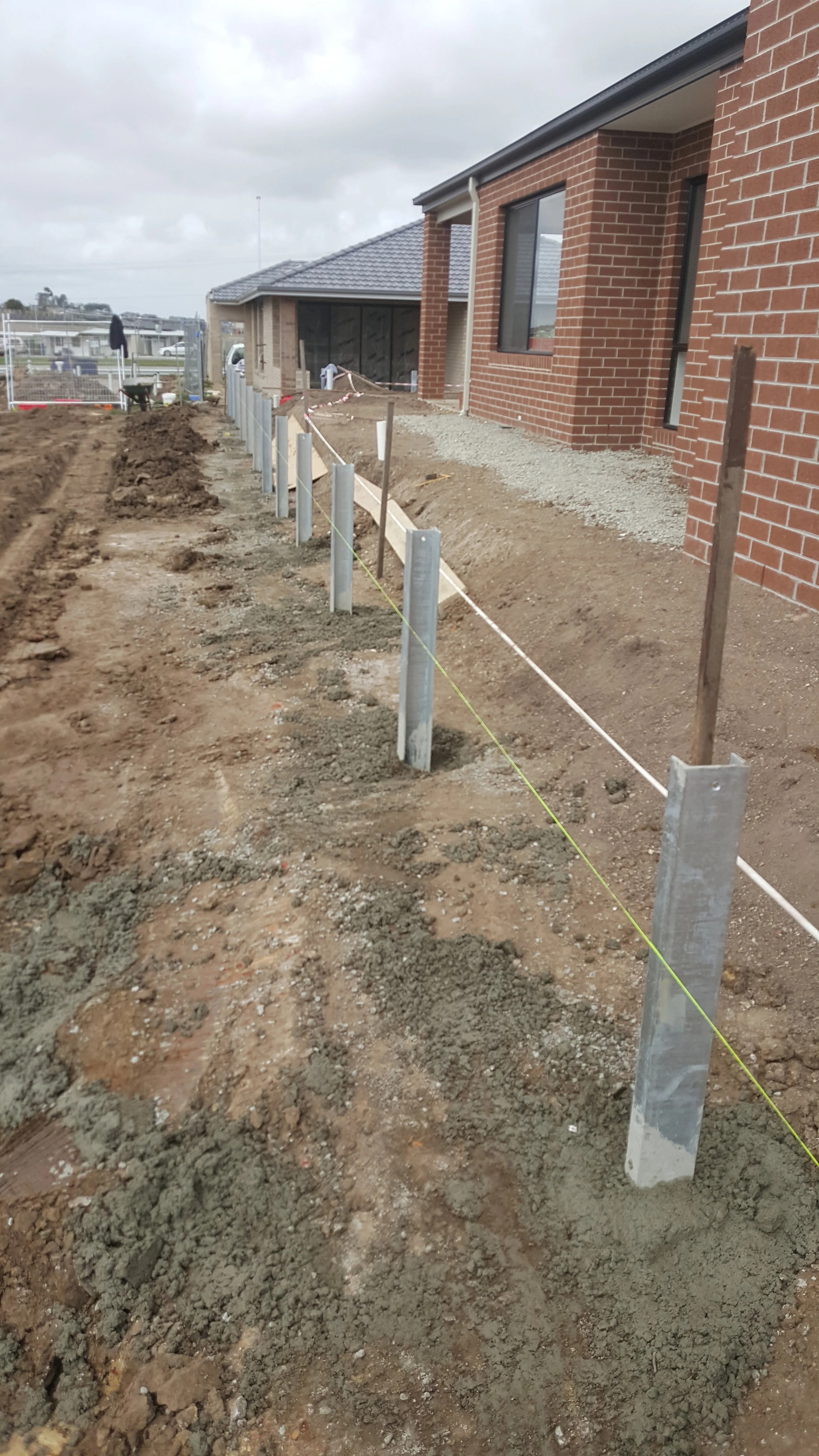 Row of steel posts set in the ground along a property boundary next to a new brick home.