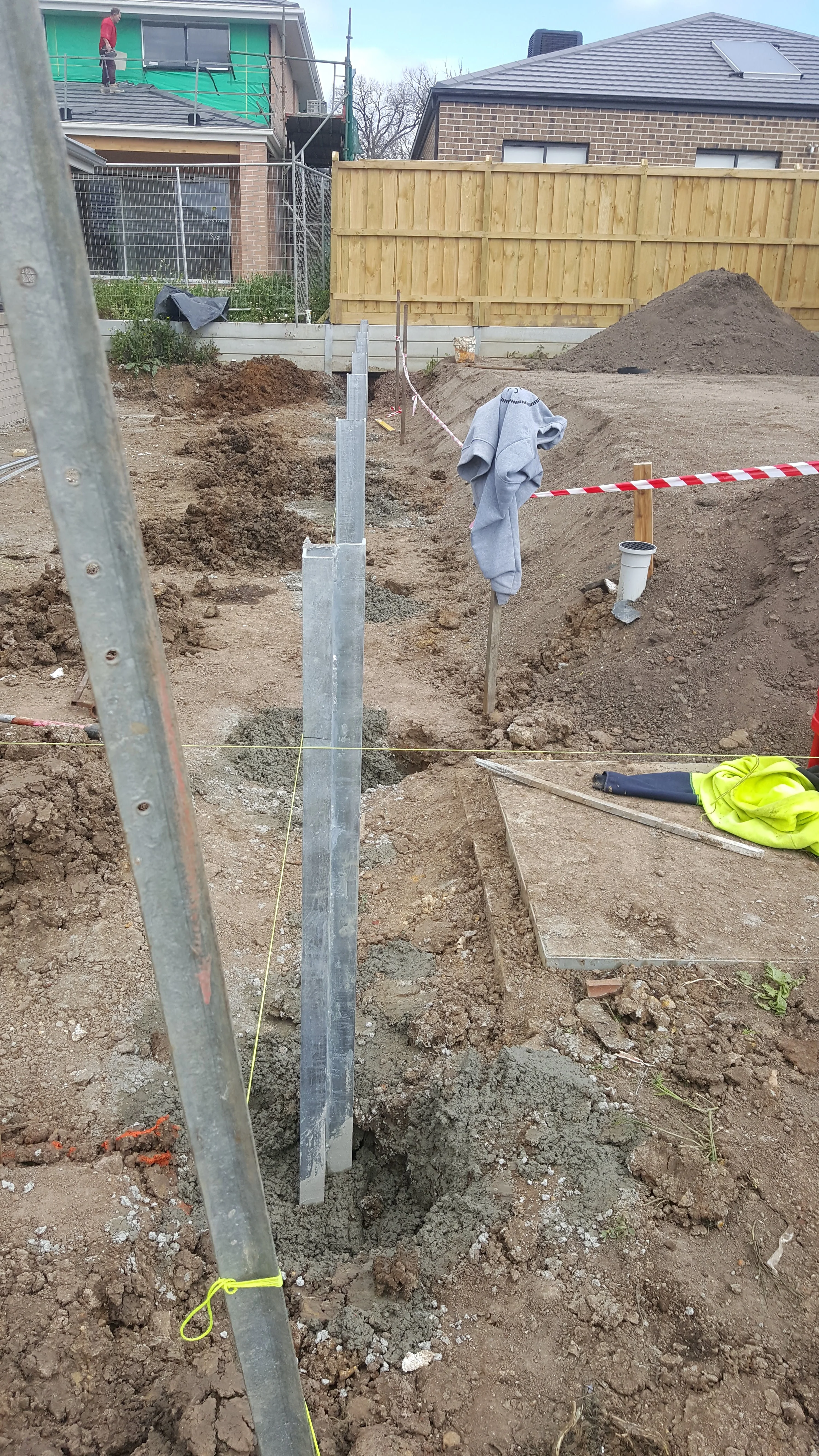 Steel posts and post holes along a boundary with a timber paling fence and new houses behind.