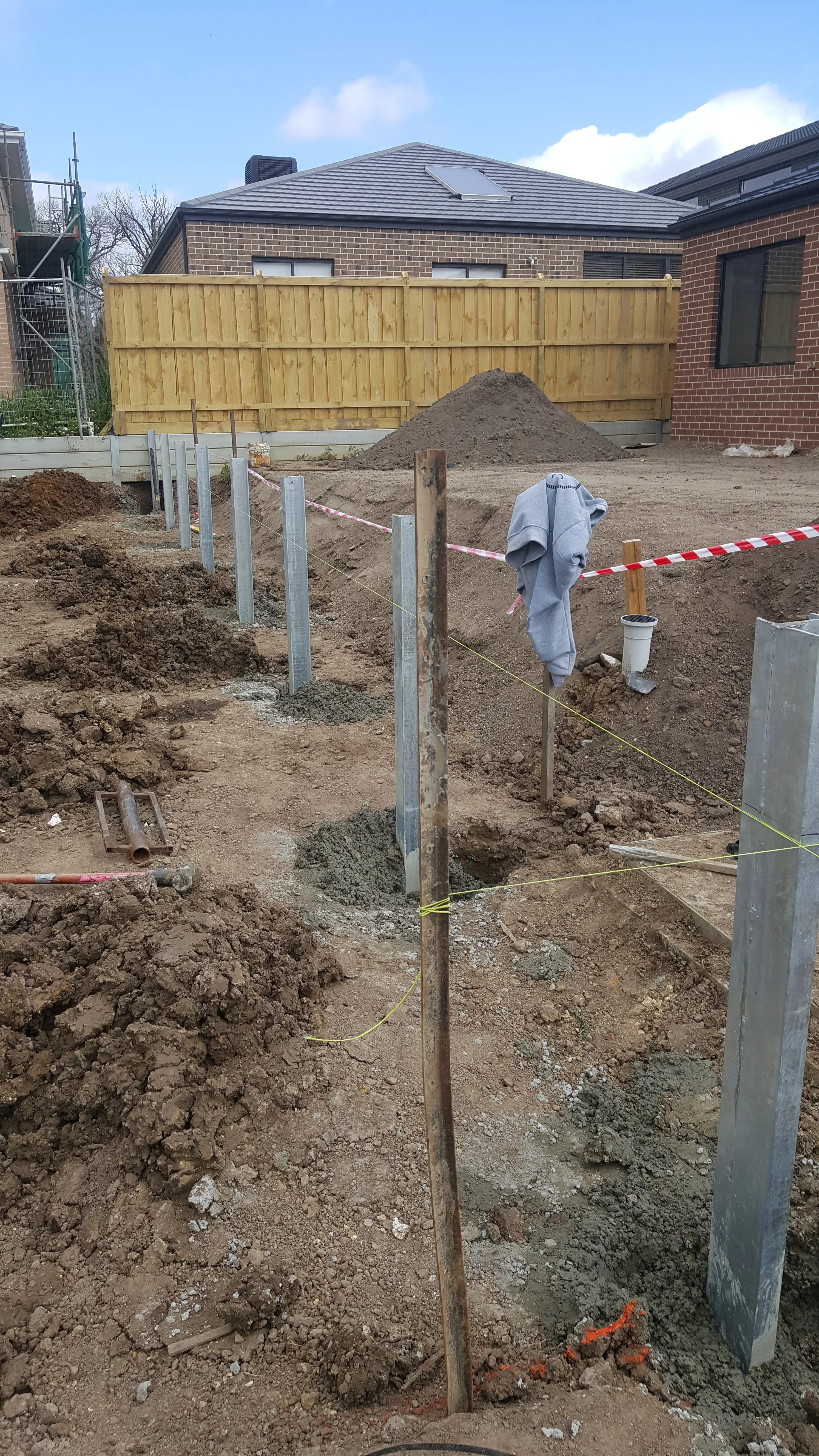 Steel posts in freshly dug ground beside a timber paling fence on a new-estate block.