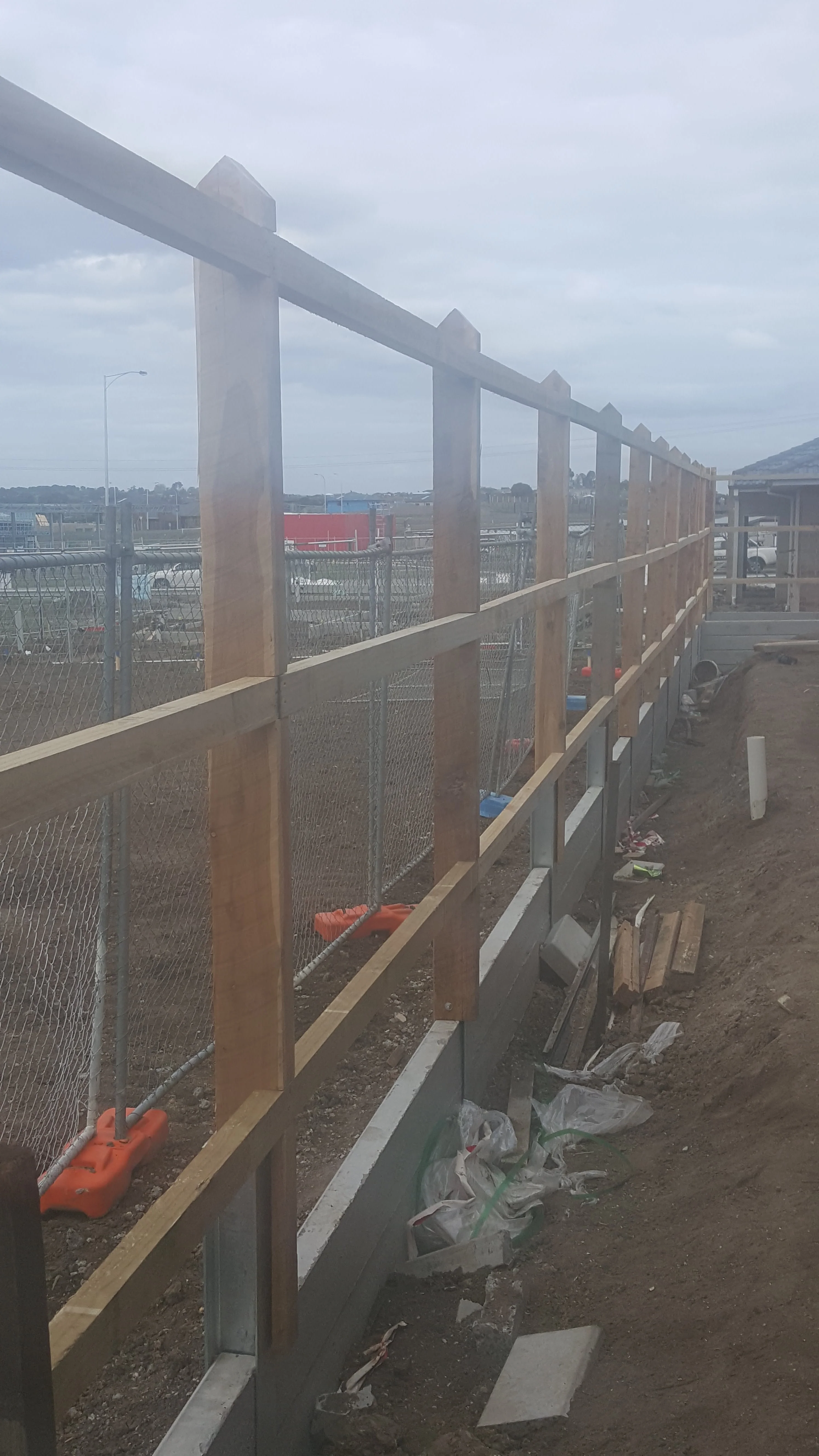 Timber fence frame with rails above grey concrete sleepers held by steel posts, looking along the boundary.
