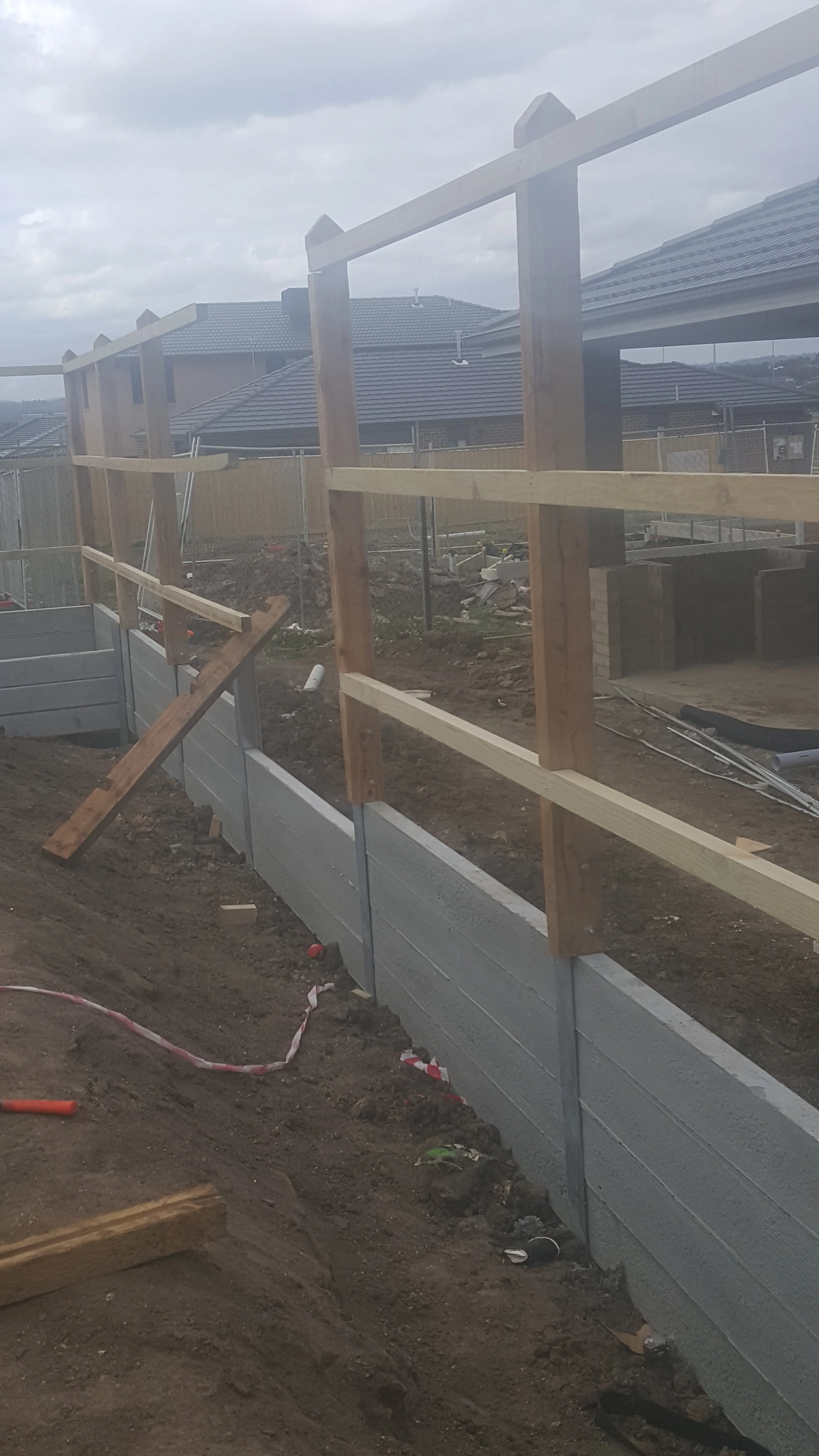 Concrete sleeper retaining wall with a timber fence frame above, shot looking along the fence line.