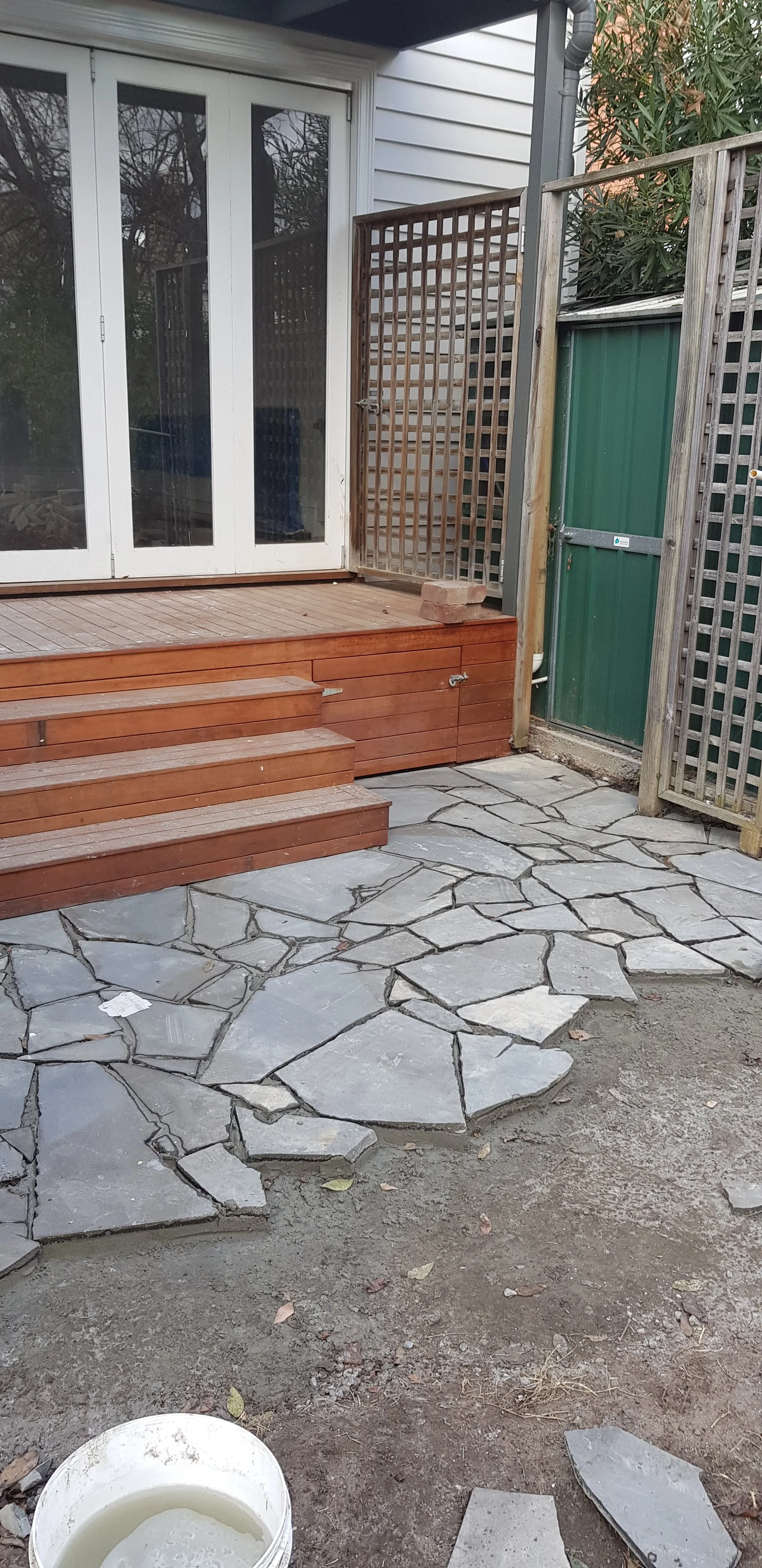 Irregular bluestone crazy paving being laid in front of red timber steps and French doors.