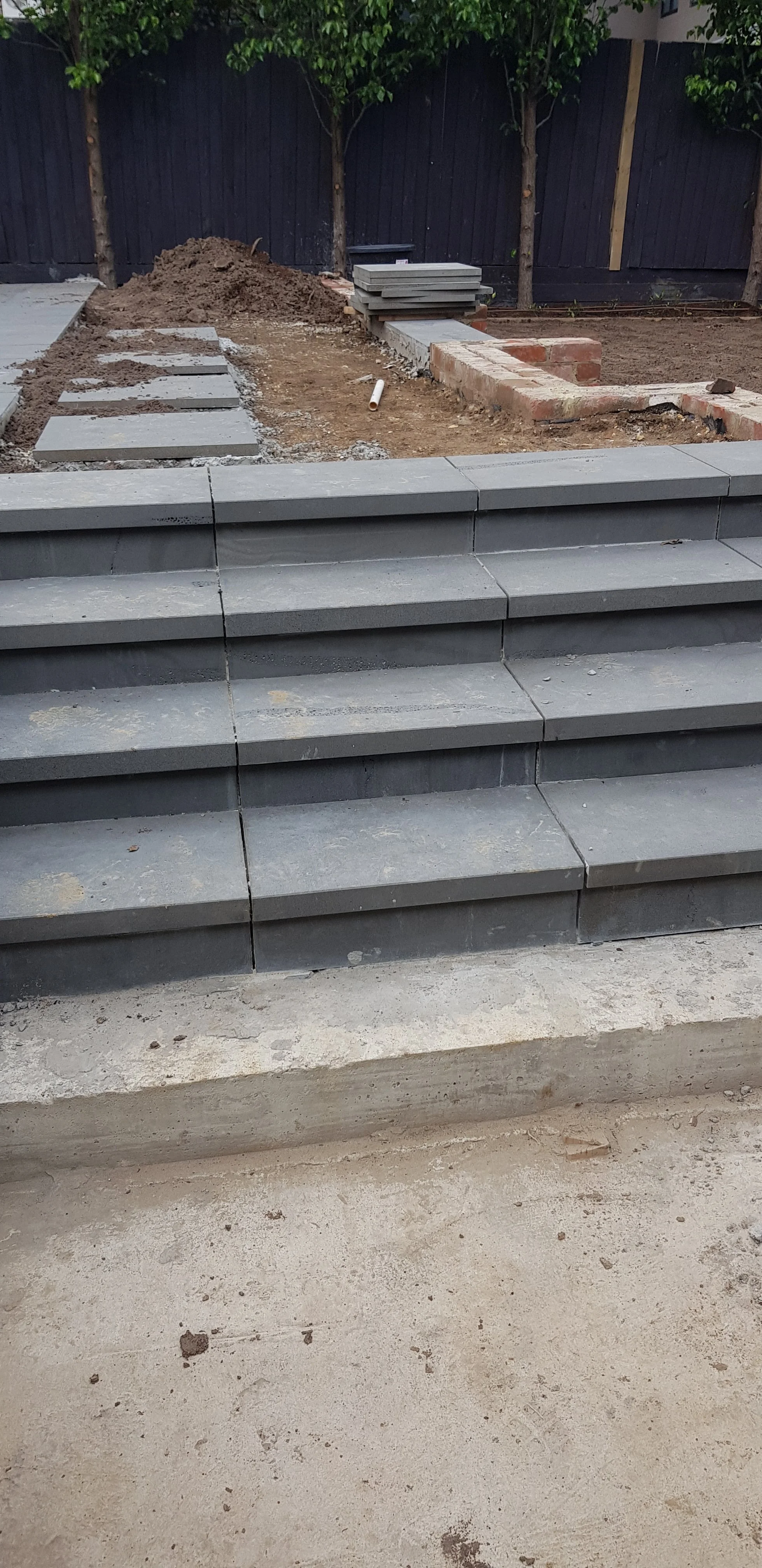 Wide grey paved steps under construction with a sand base and garden beds being formed above.