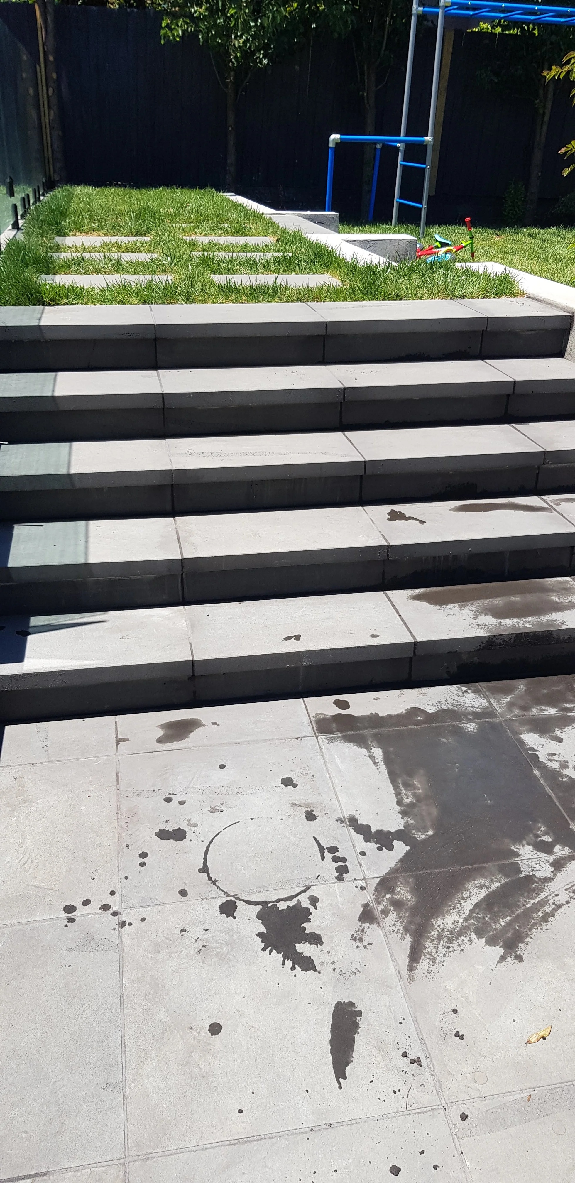 Finished grey paved steps rising from a paved area to a lawn with stepping pavers.