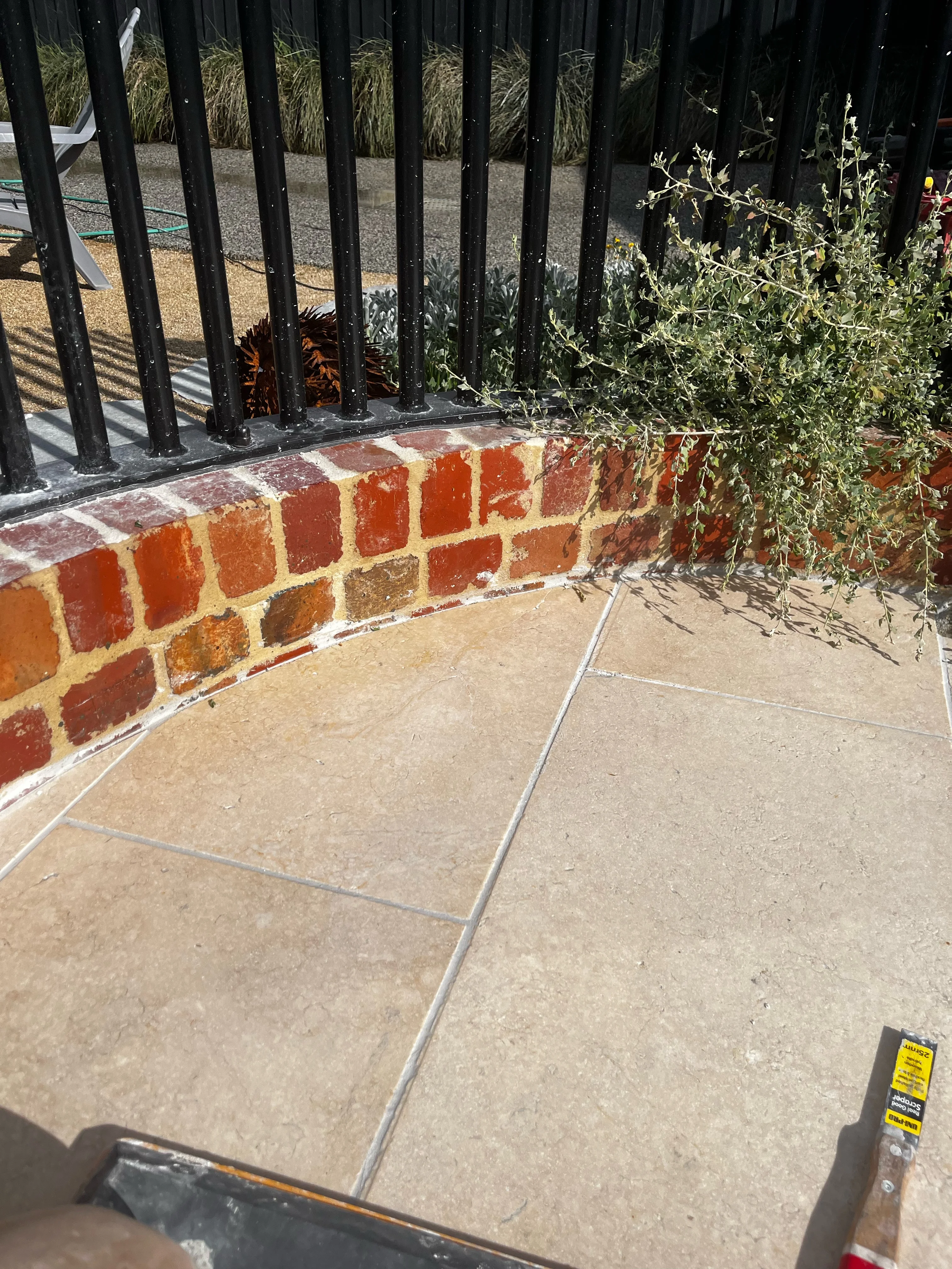 Pale stone pavers laid tight against a curved red brick planter wall.