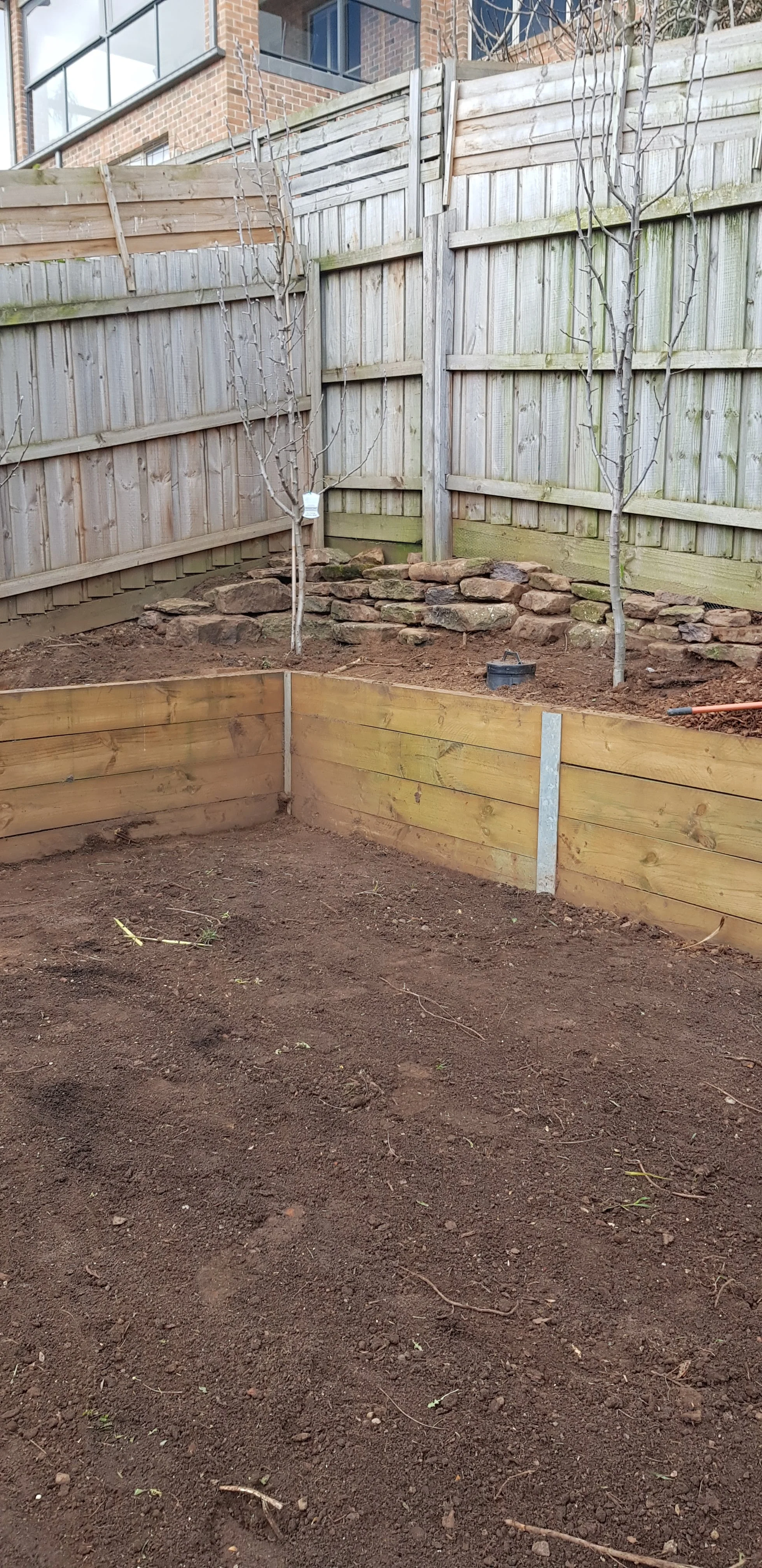 Treated pine sleeper wall forming a raised corner garden bed against a paling fence.