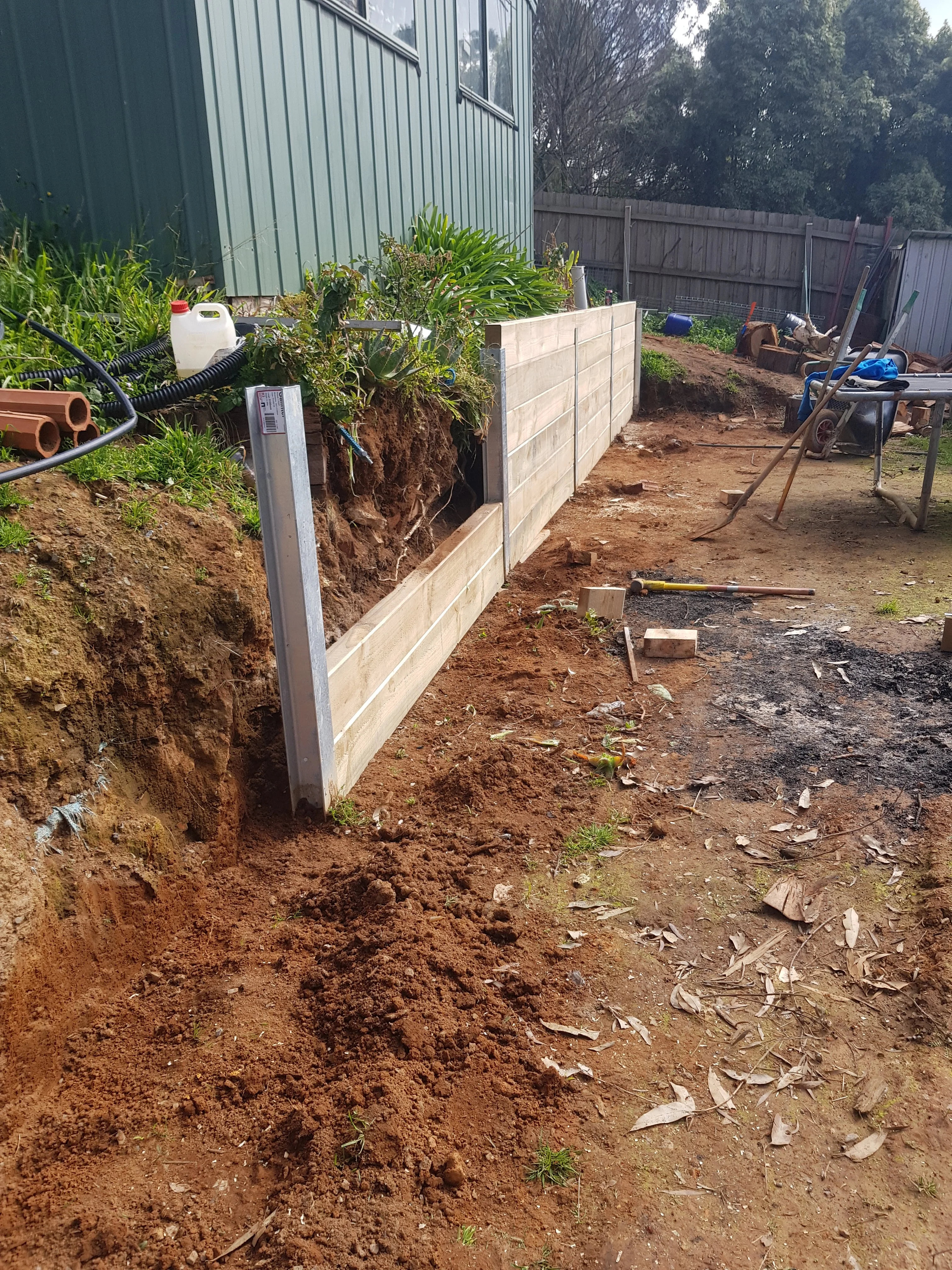 A timber sleeper retaining wall being built between steel posts to hold back a garden bank.