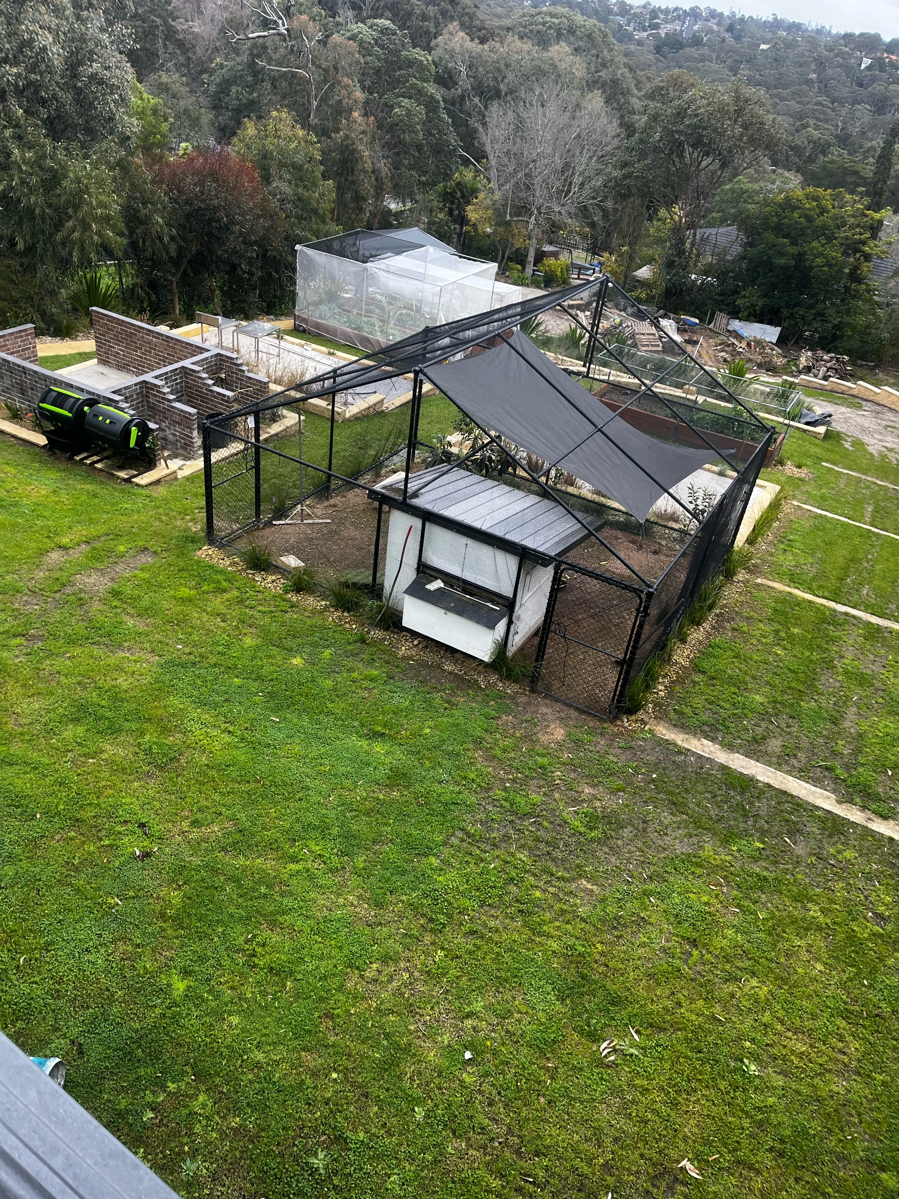 Freshly laid lawn on terraced levels with a black mesh chicken run and coop, seen from above with a bushland valley behind.