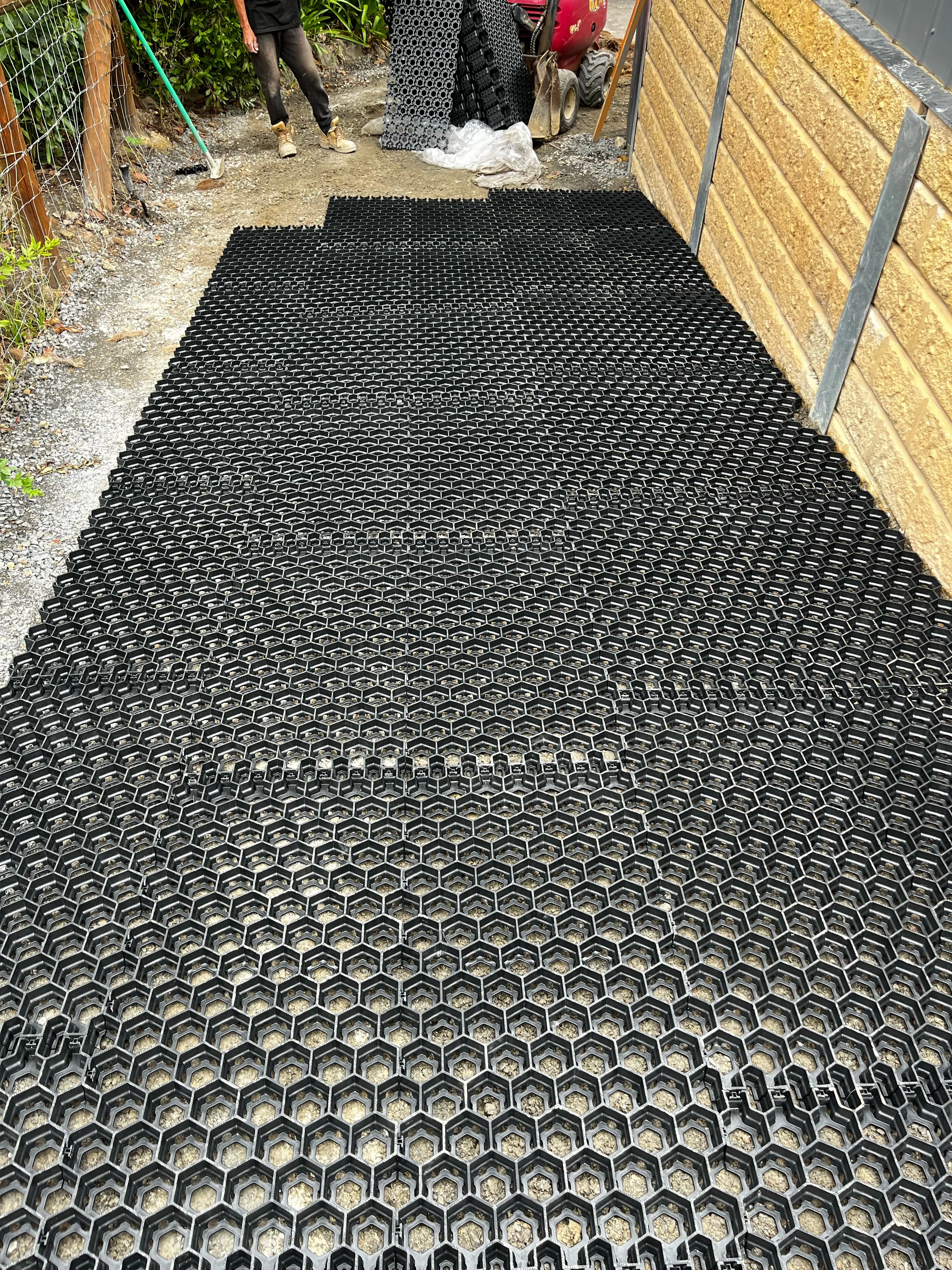 Close view of black hexagonal ground grid laid on crushed rock along a treated pine sleeper wall with steel posts.