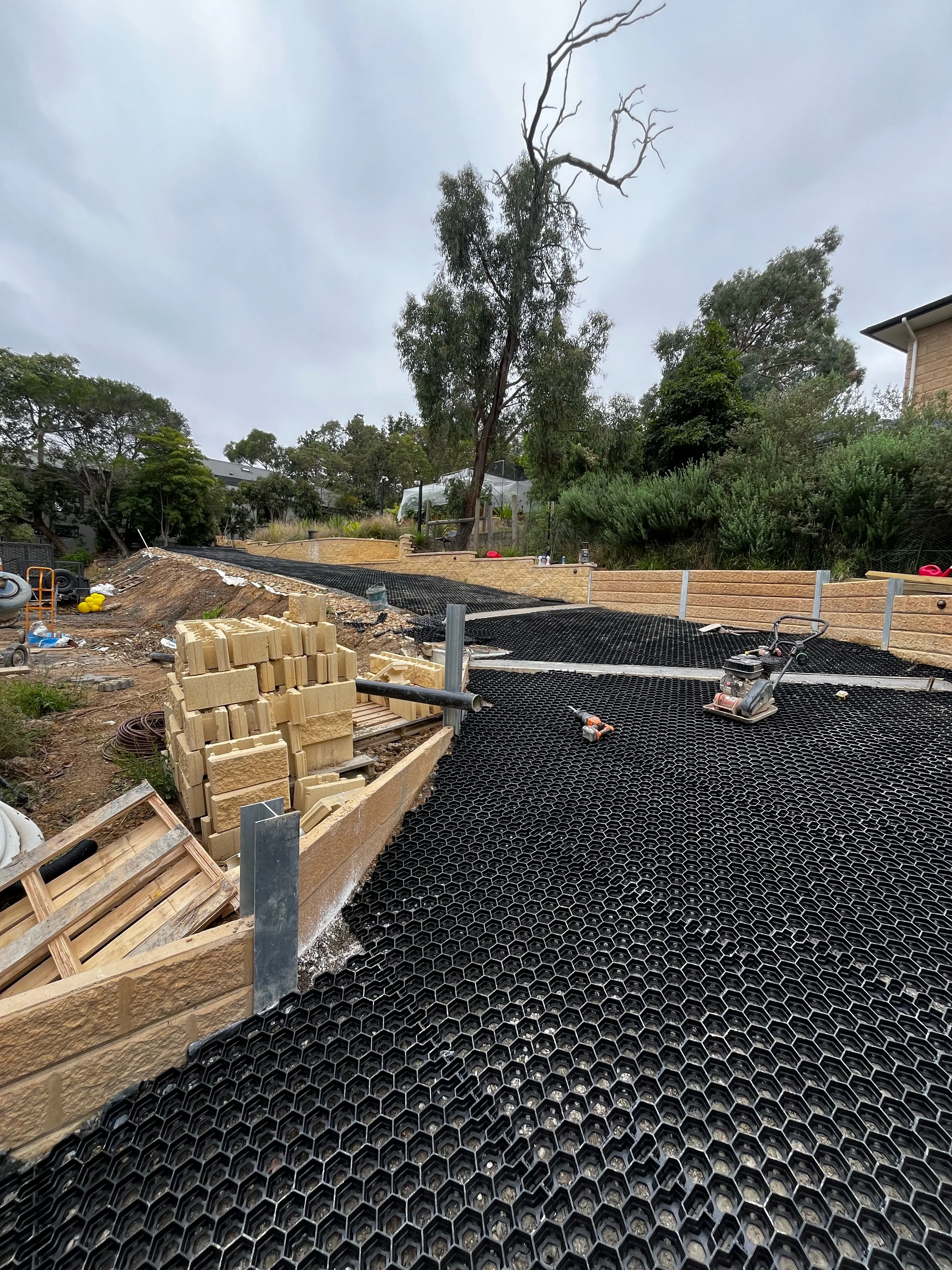 Hexagonal ground grid laid beside timber sleeper retaining walls on a graded yard.