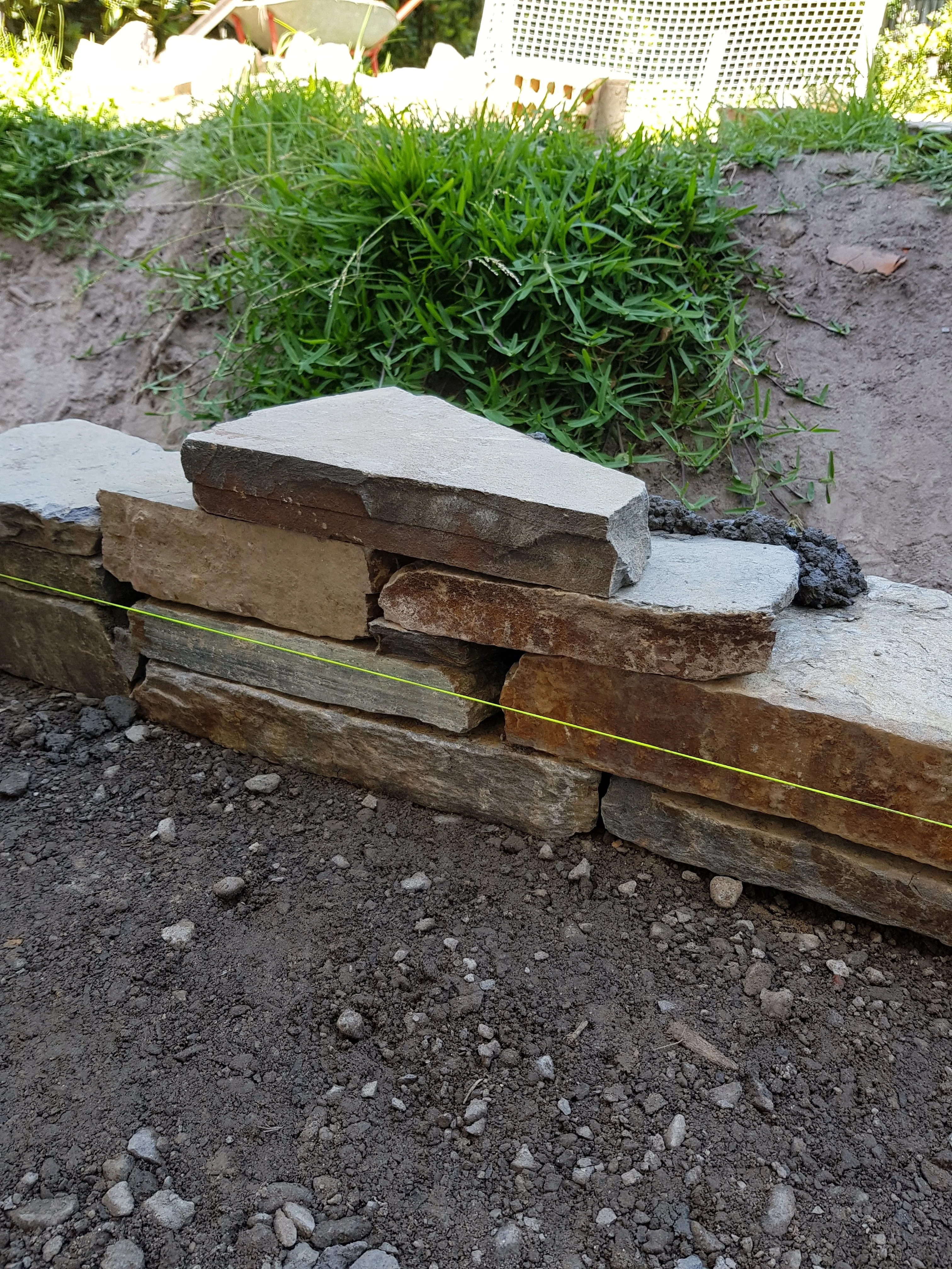 Close-up of a stacked sandstone wall with a flat capping stone, holding back a garden bed.