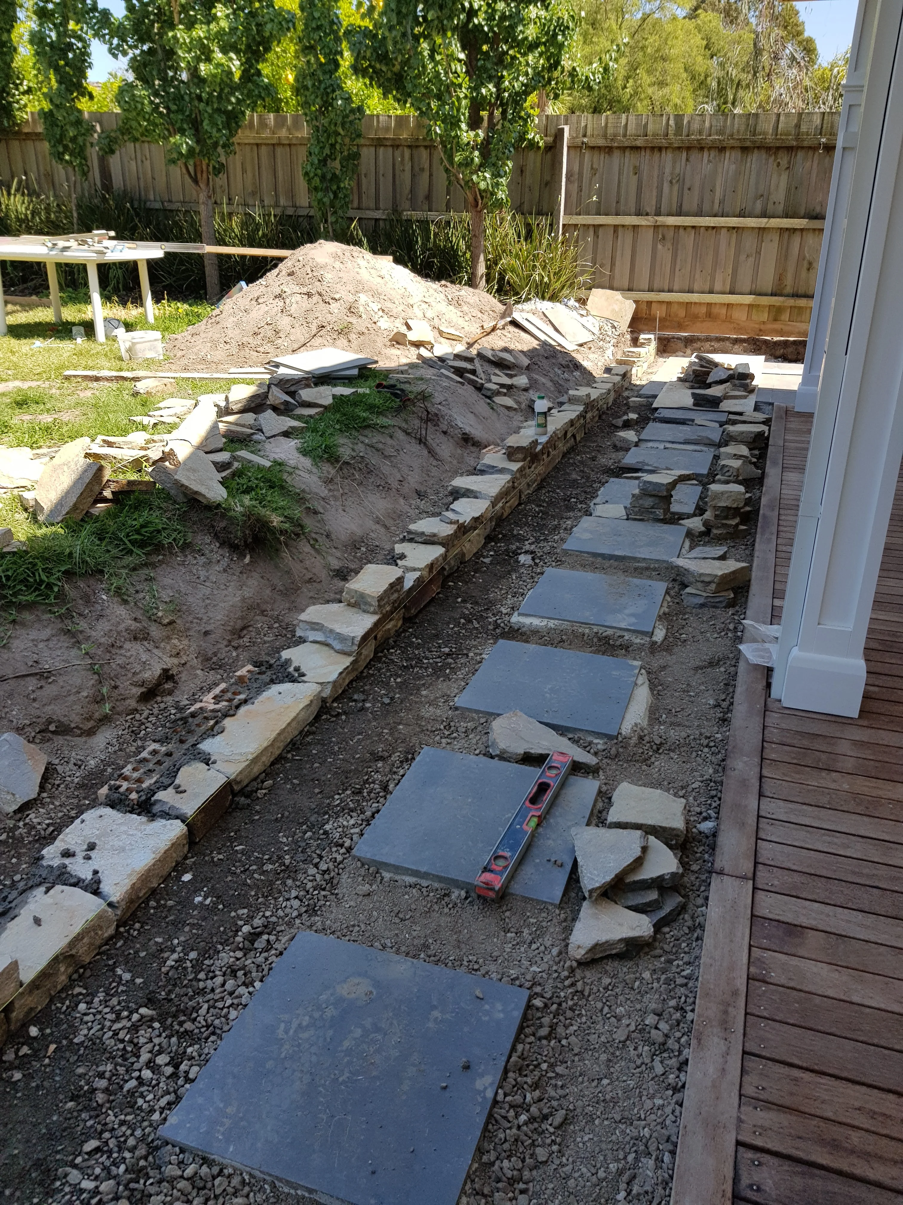 Bluestone stepping stones being laid on gravel along a side path, next to timber decking.