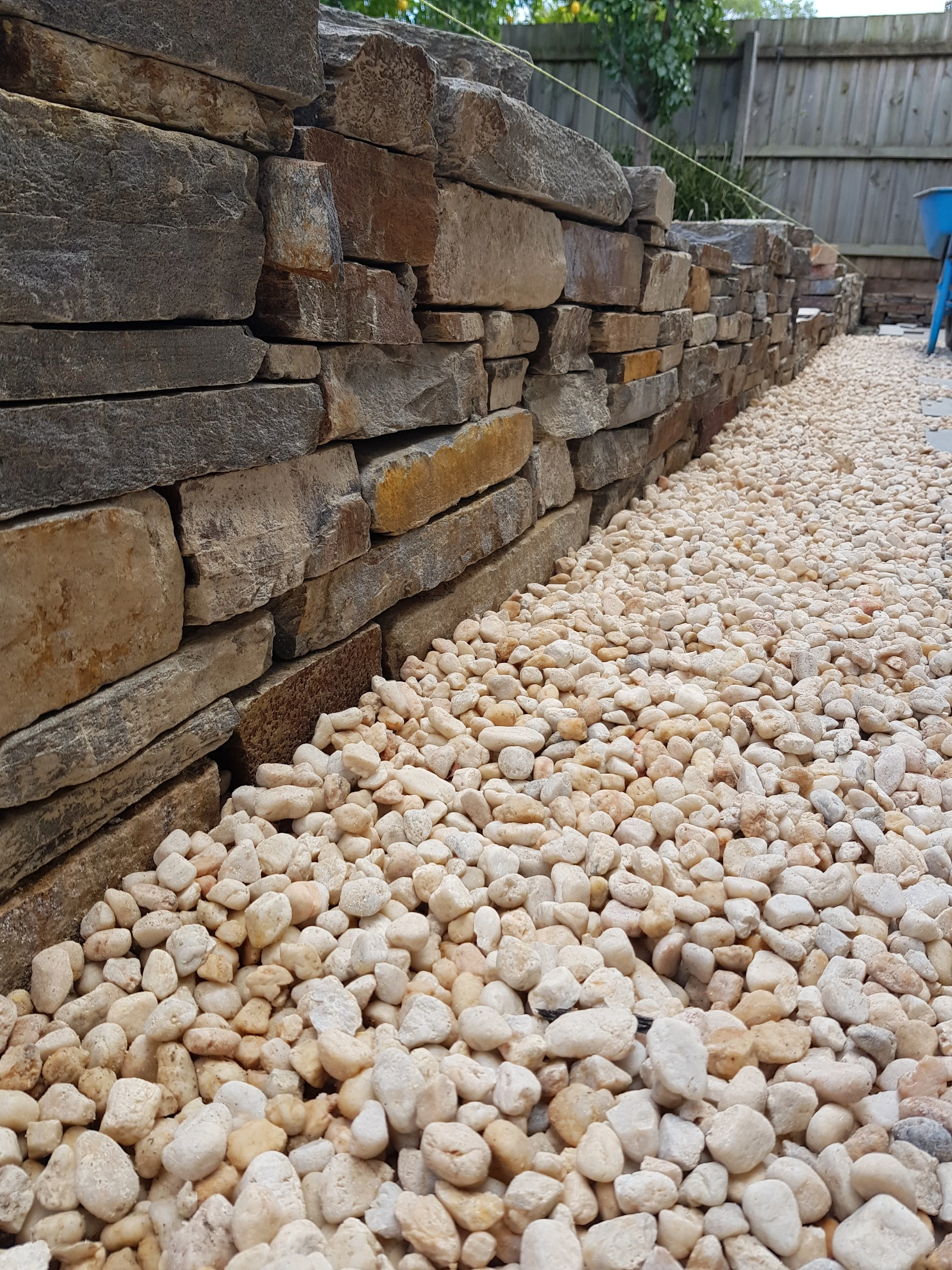 Low-angle view along a dry stacked stone wall with cream river pebbles at its base.