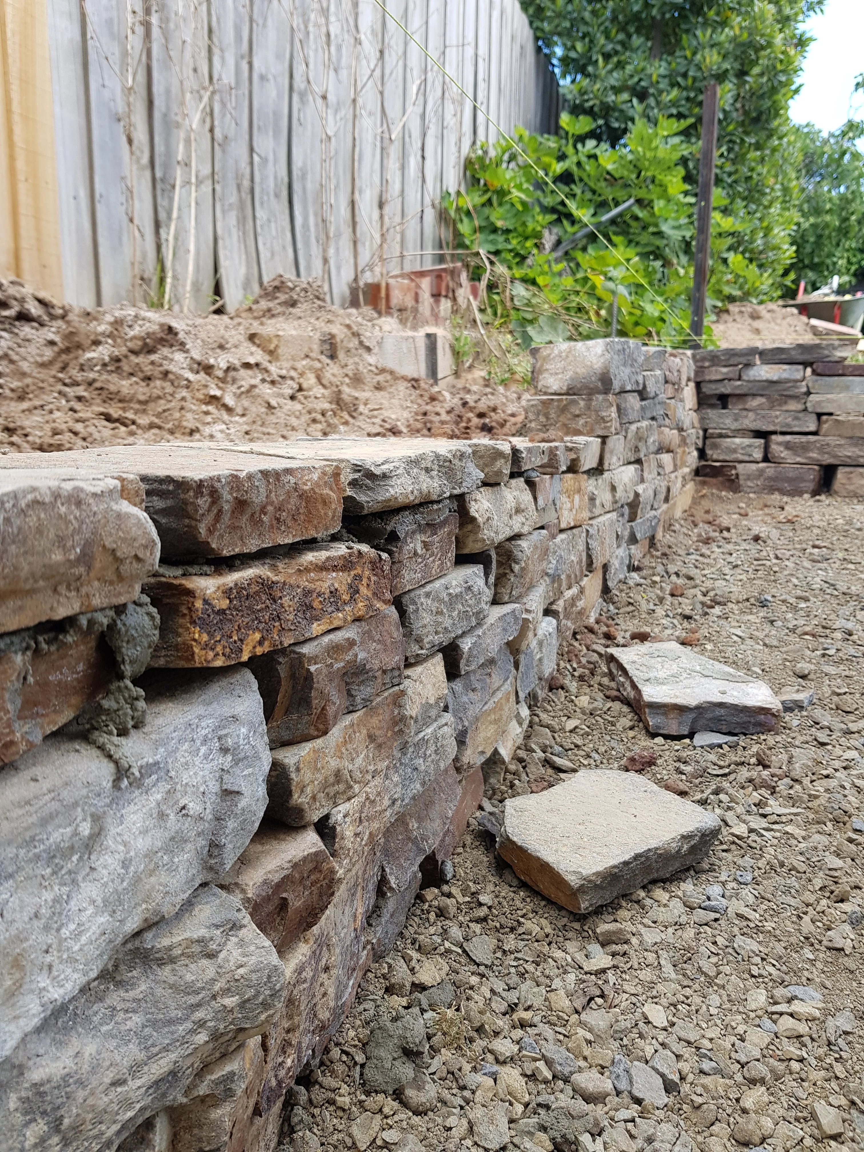 End of a dry stacked stone wall with loose stones and pebbles at its base.