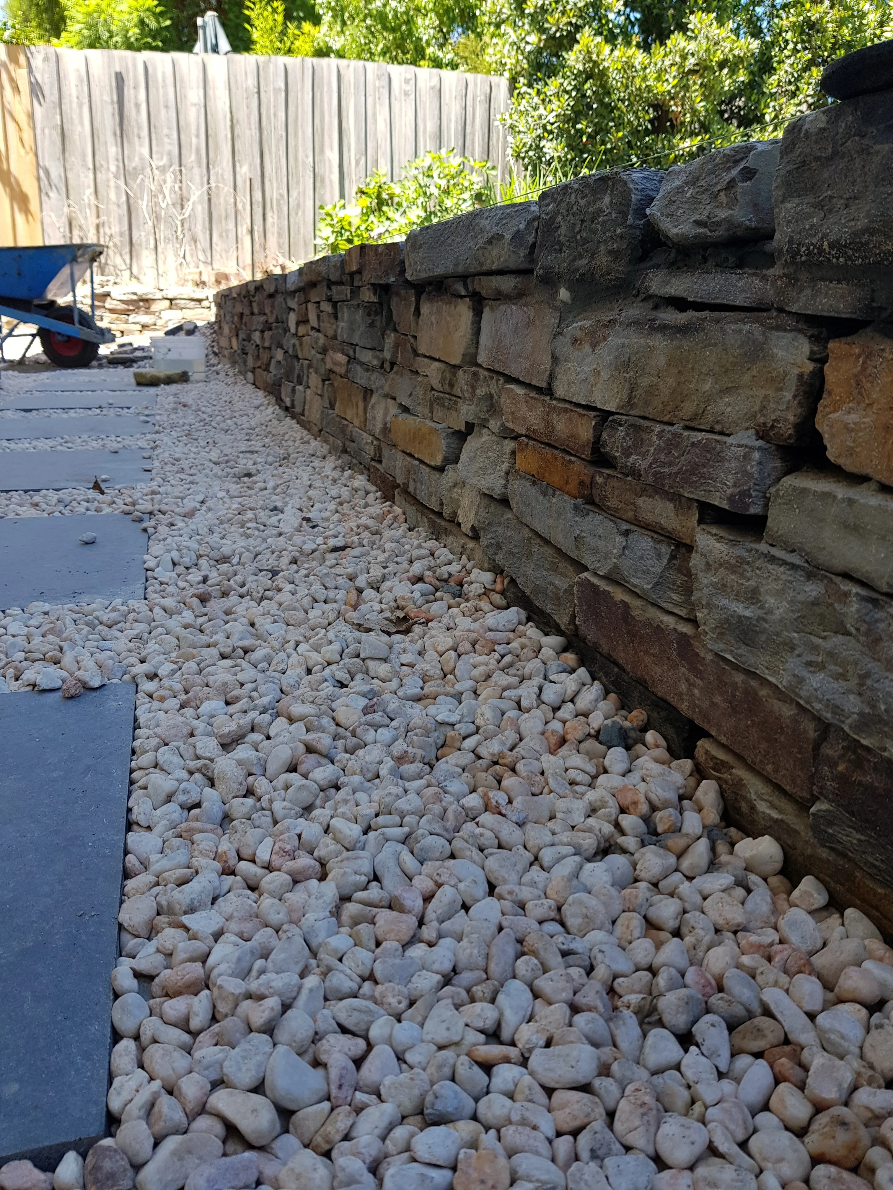 Long dry stacked stone wall running beside a cream pebble path with bluestone stepping stones.