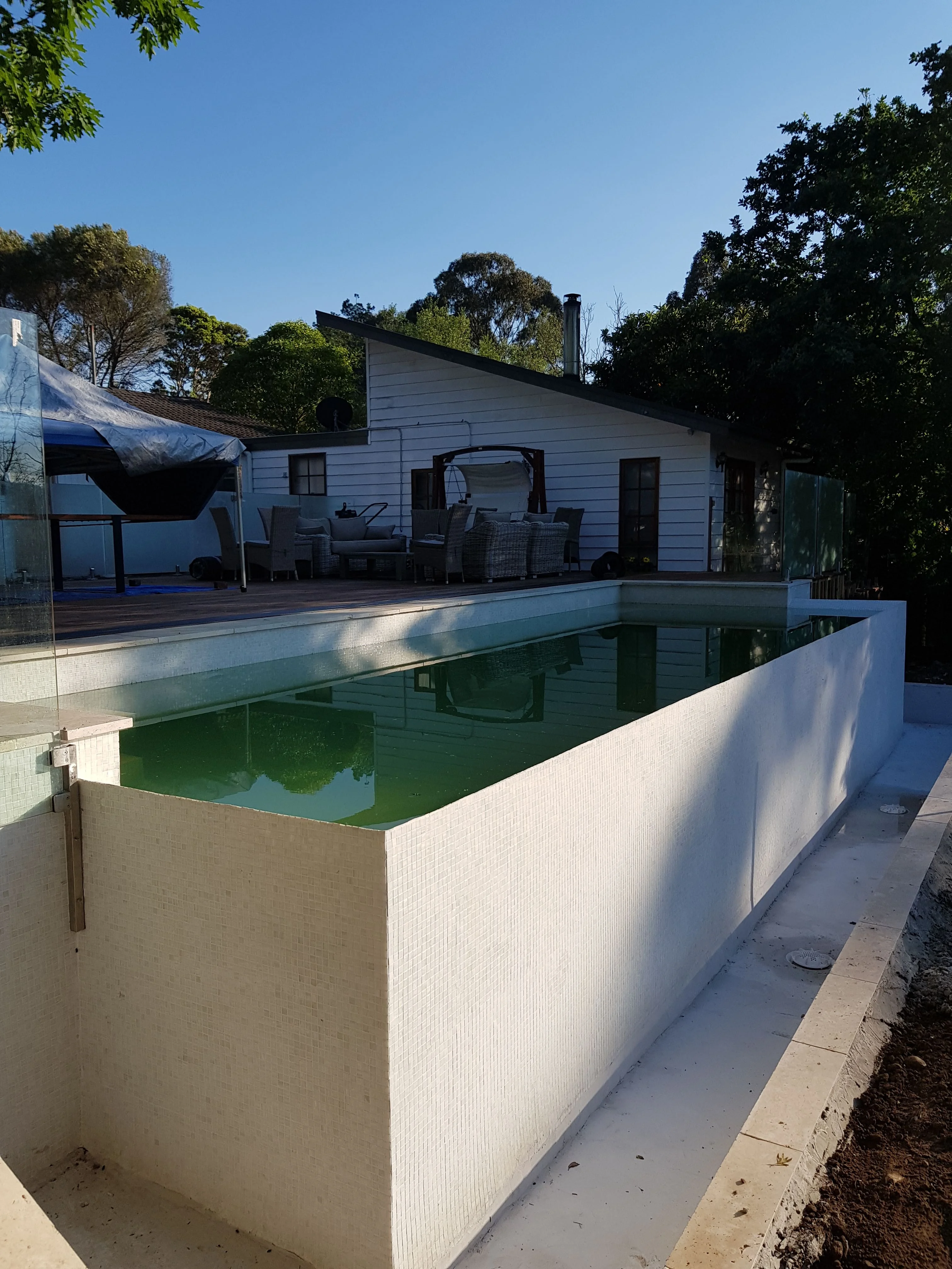 Finished raised concrete pool with smooth rendered walls, filled with water, in a backyard beside a white weatherboard house.