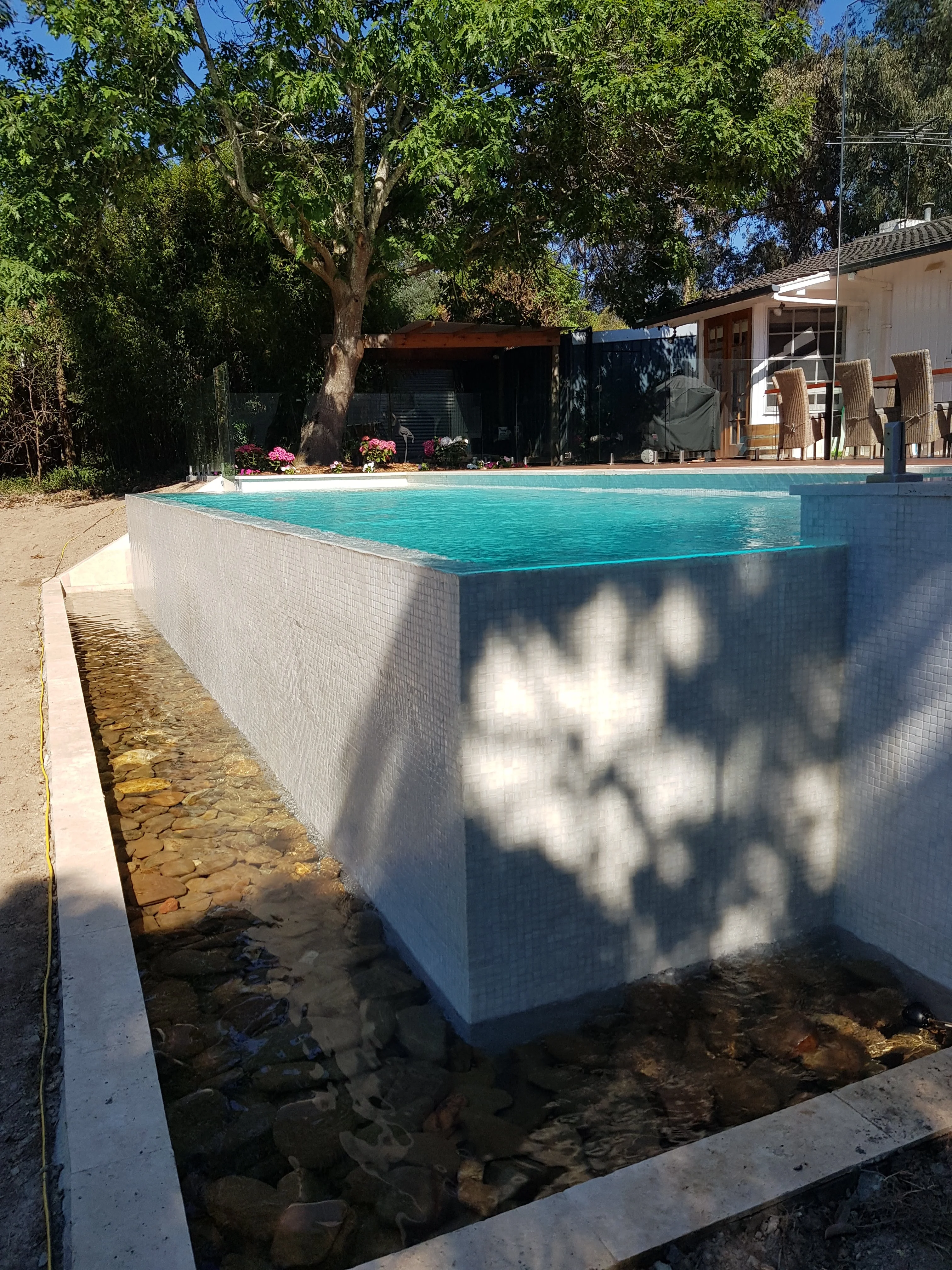 Rendered raised concrete pool with a garden edge strip around the base and trees behind.