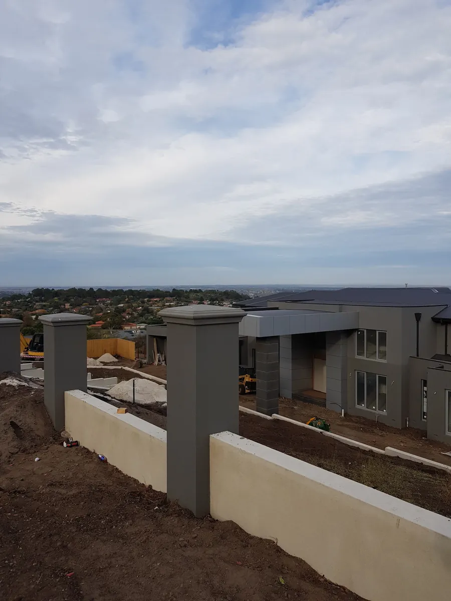 Rendered retaining wall with capped pillars on a hillside site with a wide view over rooftops