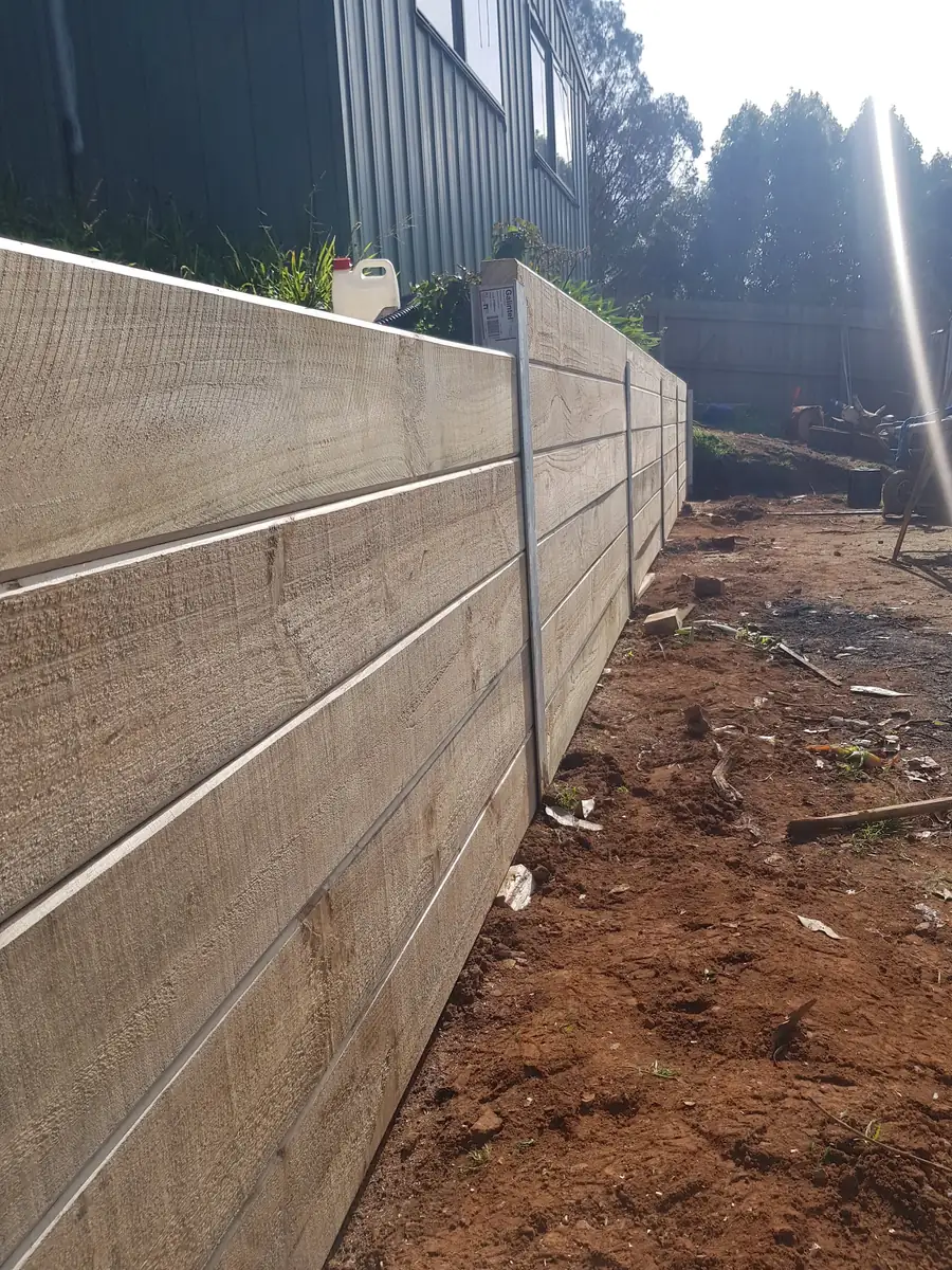 Completed horizontal timber sleeper retaining wall with steel posts in a sloping backyard