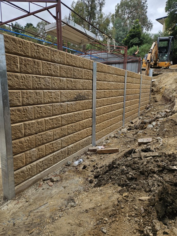 Concrete block retaining wall with steel posts under construction